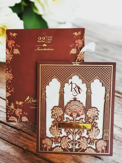 This design is for those who dream of a royal wedding. It features an incredibly detailed laser-cut MDF frame with a Mughal-inspired floral pattern, a custom monogram, and a delicate feather tassel, all in a rich maroon that speaks of luxury.
