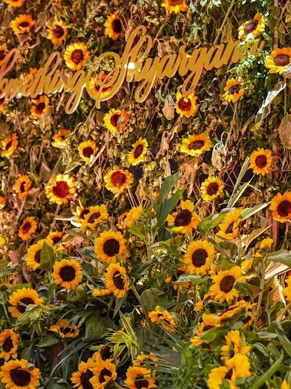 A clear, bright shot of the sunflower wall with the couple's custom hashtag. The sheer density of the flowers creates a stunning and joyful visual impact.