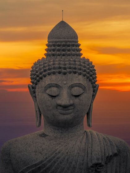 The gentle face of the Big Buddha statue in Phuket, glowing in the warm light of the setting sun.