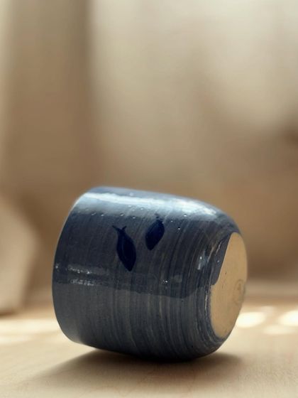 A Blue Fish Tumbler lying on its side, catching the light. The simple fish motif and the flowing lines of the marble clay give it a sense of movement and tranquility.