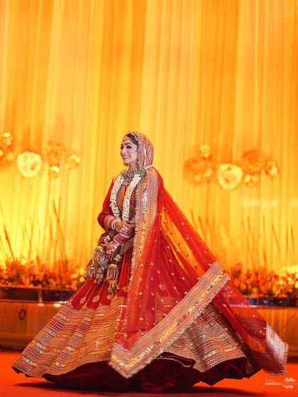 A stunning full-length shot of the bride, her red and gold lehenga catching the light beautifully. Her twirl shows off the magnificent flare of her dress, making her look like a queen.