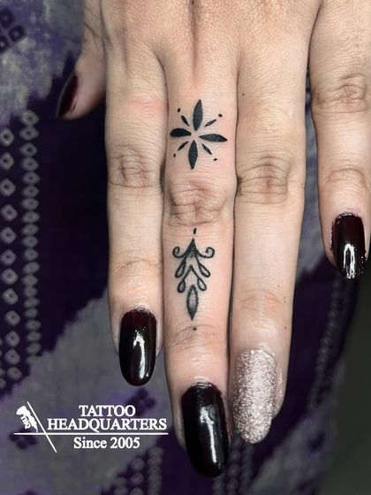 Elegant fine-line tattoos on the fingers, including a starburst and a delicate ornamental design.