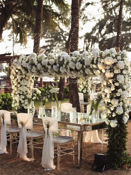 A stunning floral arch frames the dining setup for a beach wedding, allowing guests to dine with an uninterrupted view of the ocean.