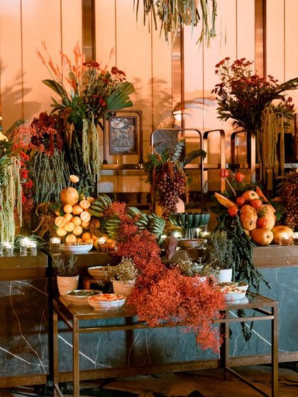 A wide shot of the grazing table, where arrangements of grapes, oranges, and even corn are seamlessly integrated with lush floral and foliage displays.