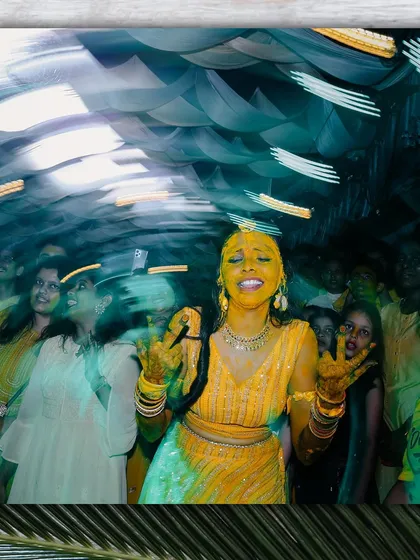 A creative shot using a slow shutter speed to capture the motion and energy of the Haldi dance floor. The bride is at the center of the celebration, glowing with joy.