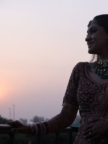 A serene bridal portrait taken during sunset. The silhouette against the warm, hazy sky creates a beautiful and contemplative mood, capturing a quiet moment before the celebrations begin.