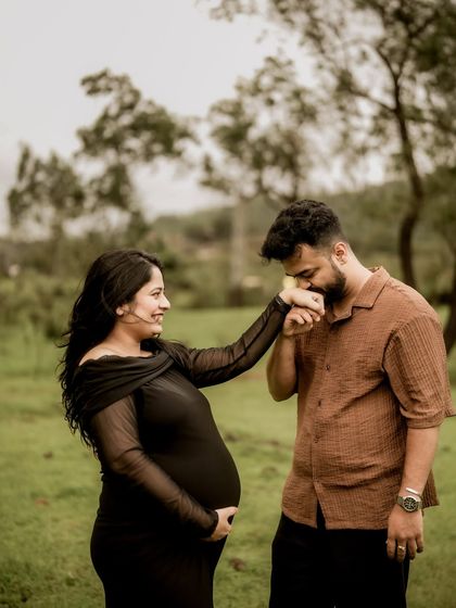 A classic romantic gesture. He gently kisses her hand as she smiles at him, a timeless expression of love and chivalry in a beautiful outdoor setting.