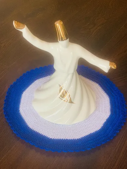 An Evil Eye-inspired placemat in shades of lavender and blue. It's a unique take on the traditional design, shown here as a base for a whirling dervish statue.