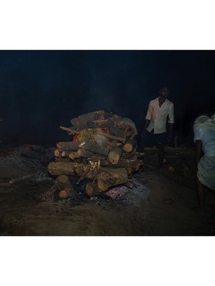 A cremation takes place at night, the fire illuminating the darkness in a cycle that never stops at this ghat.