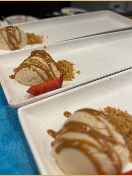 A scoop of creamy dessert, possibly a cheesecake mousse, drizzled with caramel sauce and served with a crumble for texture. A simple, yet sophisticated sweet course.