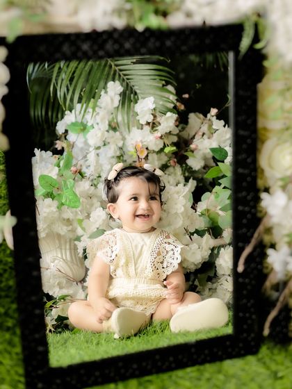 A joyful baby framed by a mirror and surrounded by white flowers. This creative composition adds depth and artistry to the portrait.