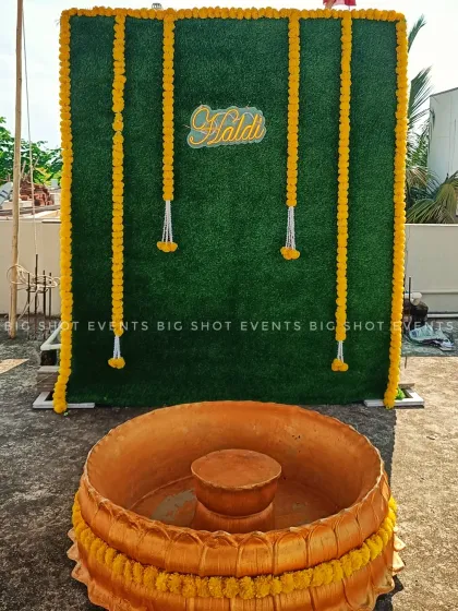 A simple yet elegant Haldi decoration for a terrace event. We used a green turf wall as the backdrop, decorated with vertical strings of yellow marigolds and a custom "Haldi" sign, with a traditional golden basin placed in front.