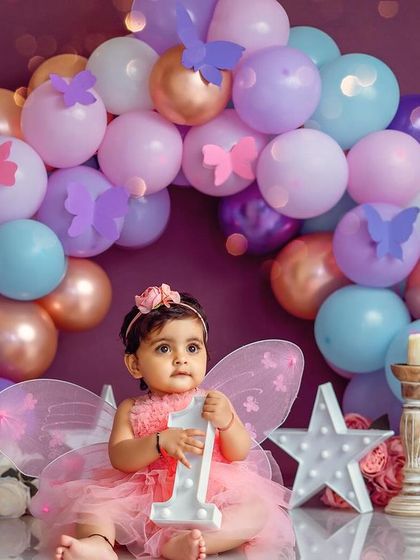 A little butterfly celebrating her first year. The pastel balloon arch and fairy wings make this a truly enchanting birthday portrait.