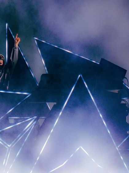 A side view of Alan Walker on his unique, angular stage, surrounded by blue light and smoke.