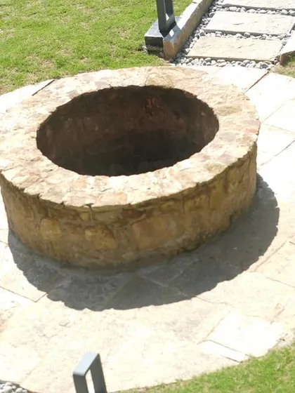 A high-angle shot of the stone well, emphasizing the circular paved area around it and its placement within the lawn.