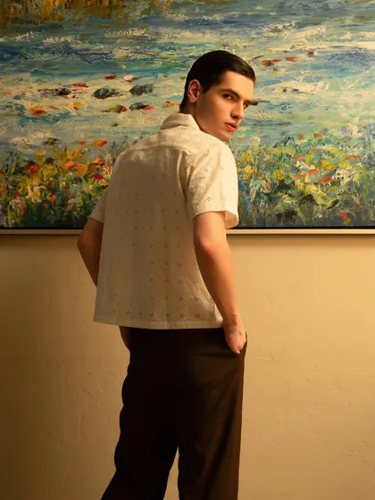 An artistic shot for a menswear lookbook, using a painting as a colorful backdrop. The model's pose, looking back over his shoulder, is dynamic and engaging.