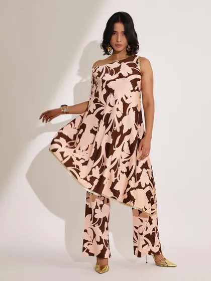 An asymmetrical printed tunic paired with matching trousers. The styling is fluid and contemporary, with gold accessories adding a touch of warmth to the brown and pink print.