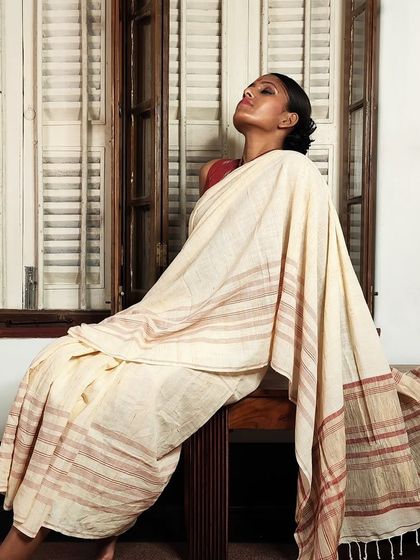 A model relaxes in a classic cream and red handloom cotton sari, showcasing its effortless grace and comfort.