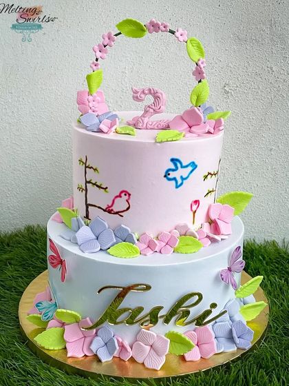 A beautiful two-tier cake decorated with pastel flowers and hand-painted birds. The delicate floral arch on top adds a touch of elegance.