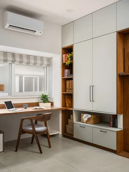 A view of the 'Palaash' home office with the Murphy bed folded away. The design seamlessly integrates a full-sized wardrobe, open shelving, and a spacious work desk that runs along the window.