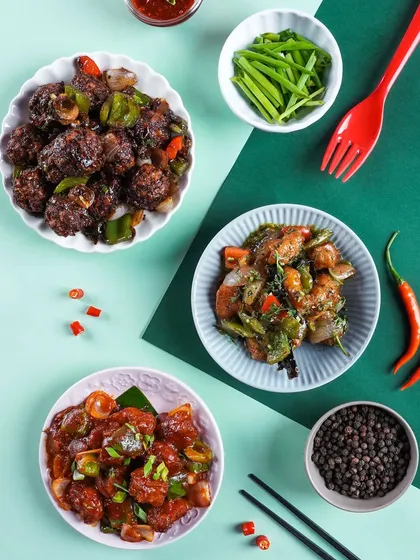 A flatlay of various Indo-Chinese appetizers like chili paneer and gobi manchurian. The geometric composition and color-blocked background create a modern and graphic visual.