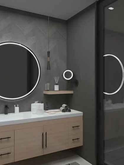 A modern bathroom with dark grey textured walls and a round backlit mirror. The light wood vanity adds a touch of warmth to the cool-toned space.