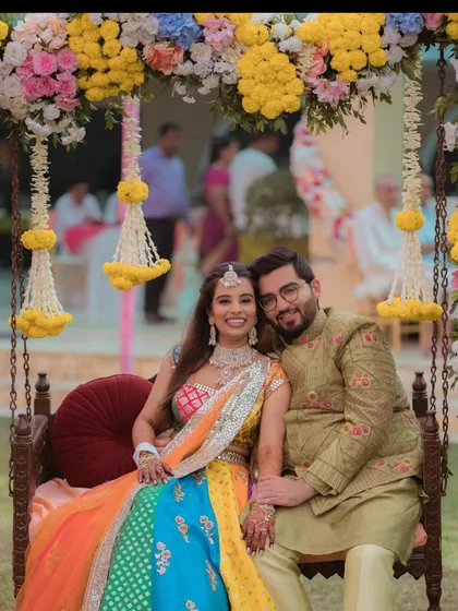 A happy couple enjoying their Mehendi ceremony on a beautifully decorated swing. The swing is adorned with colorful flowers and traditional hangings, making it a perfect photo spot.
