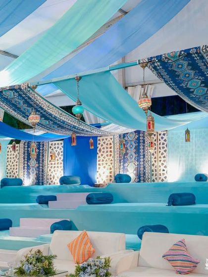 A relaxed seating area with a cool blue color palette. The multi-level seating is adorned with blue cushions and set under a ceiling of blue and white drapes, creating a serene atmosphere.