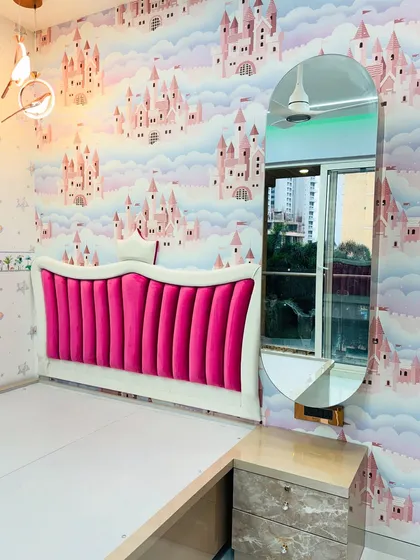 A glimpse into a princess-themed kids' bedroom I completed. The design features a vibrant pink upholstered headboard against a castle-themed wallpaper, a floating dressing table with an oval mirror, and coordinated furniture.