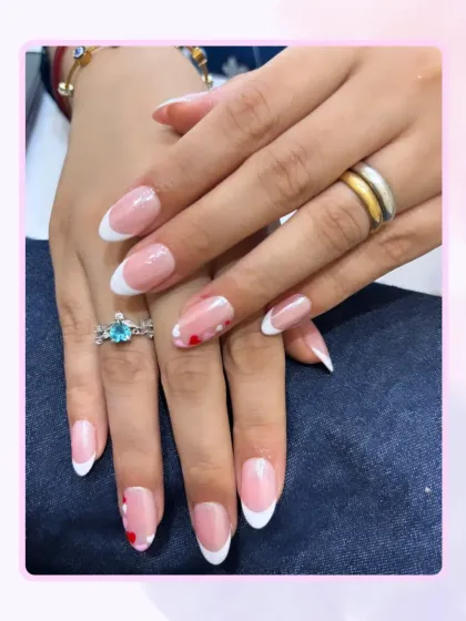 A fresh take on a classic. This is a beautiful French manicure on almond-shaped nails, with a playful twist of tiny, hand-painted red hearts on the accent nails for a touch of personality.