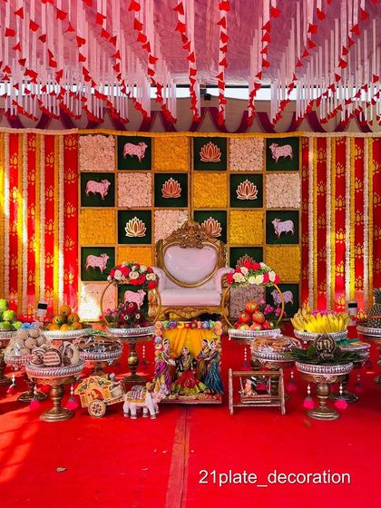 A festive outdoor baby shower setup with a red, yellow, and green theme. The decor includes a canopy, a checkered backdrop with cow motifs, and a full display of traditional items.