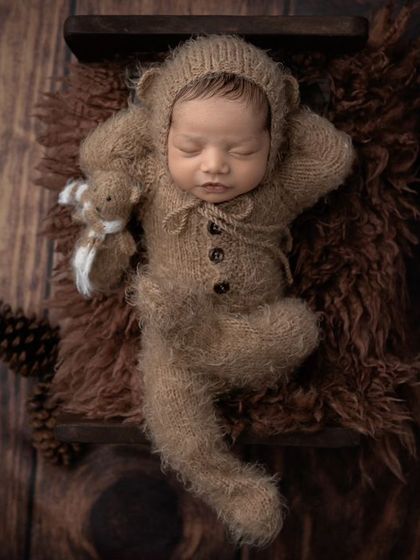 A sleepy bear cub nestled on a rustic wooden background. The textures of the wood, fur, and knitted outfit add so much depth to this newborn photo.
