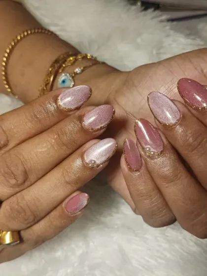 A sophisticated look featuring a shimmery pink cat-eye polish, gold glitter-lined tips, and delicate pearl and rhinestone accents.