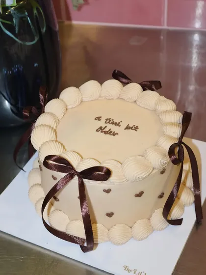 Mocha dreams baked to life. This Belgian chocolate cake is decorated with classic shell piping, tiny hearts, and rich brown ribbons for a sophisticated and indulgent treat.