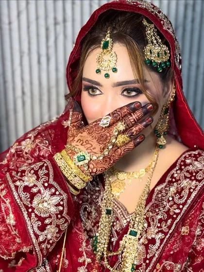 This is the same Nikkah bride, showcasing the complete look with her heavy jewelry and traditional red dupatta. The makeup was designed to be bold enough to balance the ornate details of her attire.