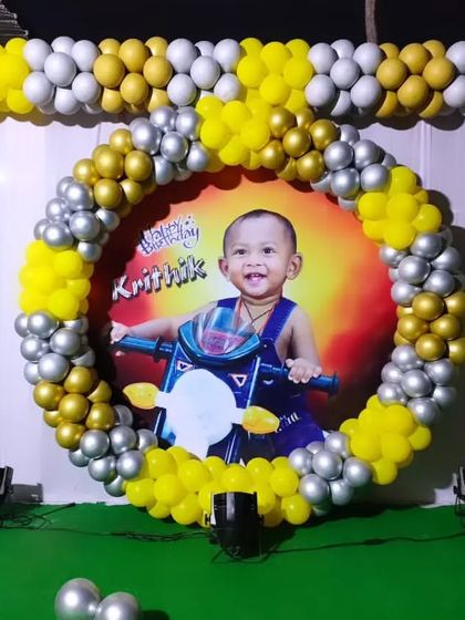 A first birthday backdrop with a personalized photo of the birthday boy, framed by a yellow, silver, and gold balloon arch.