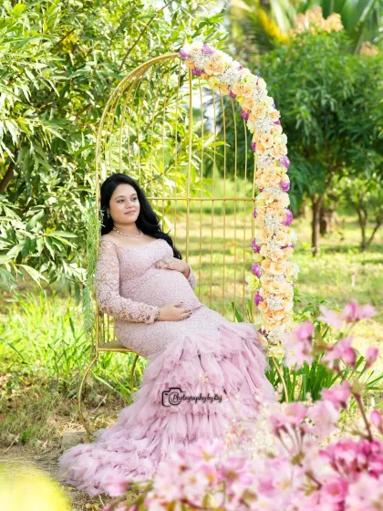 A serene moment in our garden, with the mother-to-be seated on a golden birdcage chair adorned with flowers, wearing a beautiful pink lace gown.