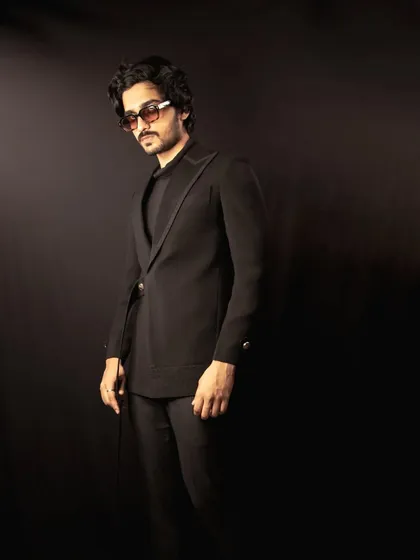 This all-black ensemble features an asymmetric jacket with a subtle glitter detail on the lapel. It's a modern, edgy take on formal wear, designed for making an entrance.