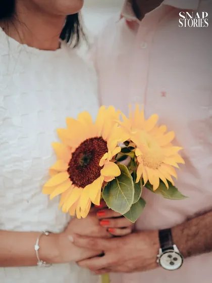 A detail shot focusing on the couple's hands holding a bouquet of sunflowers, a simple yet meaningful image that adds a personal touch to their pre-wedding story.