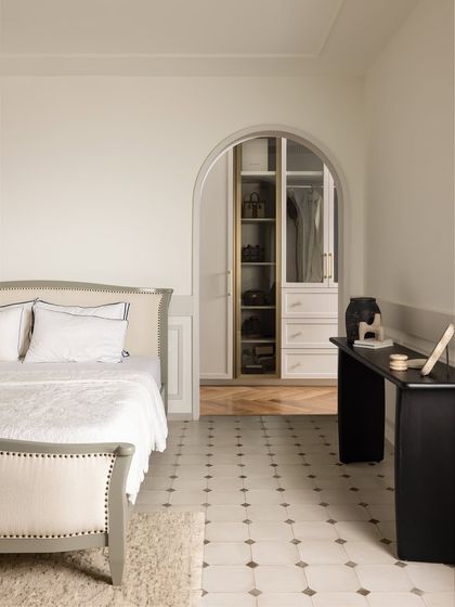 A view of the master bedroom, showing the custom-designed bed with its upholstered, curved headboard and footboard. An arched doorway leads to a spacious walk-in closet, creating a seamless suite.