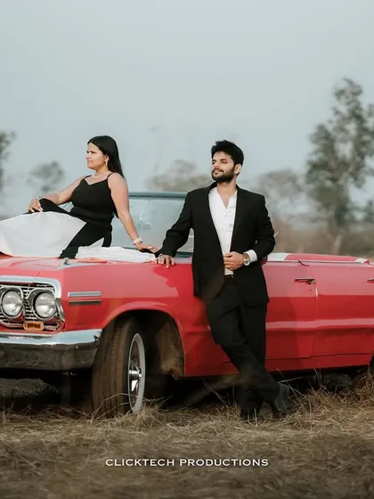 A stylish couple poses with a classic red convertible for their vintage-themed pre-wedding shoot in a rustic Goan landscape. This showcases how we can incorporate unique props to tell your story.