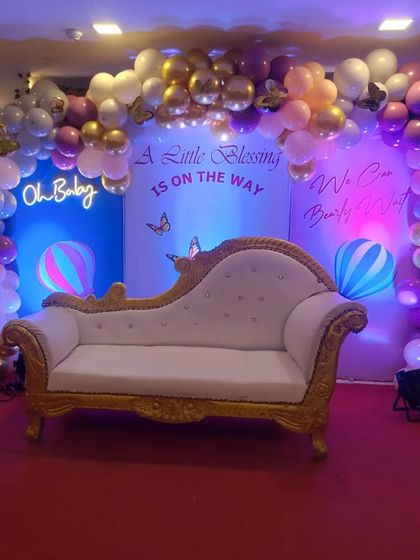 A whimsical 'A Little Blessing is on the Way' baby shower theme. The decor features a pastel balloon arch, an 'Oh Baby' neon sign, and hot air balloon cutouts against a blue backdrop.