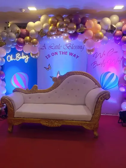 A whimsical 'A Little Blessing is on the Way' baby shower theme. The decor features a pastel balloon arch, an 'Oh Baby' neon sign, and hot air balloon cutouts against a blue backdrop.