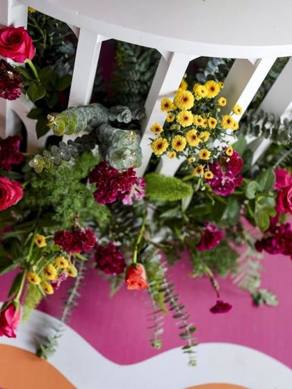 An overhead shot of a floral arrangement cascading down from a white bench, set against the vibrant pink and orange floor.
