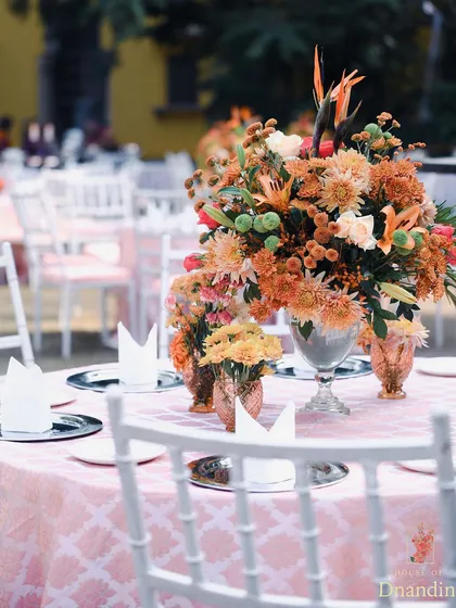 A dining table at the garden Mehendi, showcasing the beautiful crockery and the lush floral centerpiece. The silver charger plates provide a modern contrast to the soft pink linens.