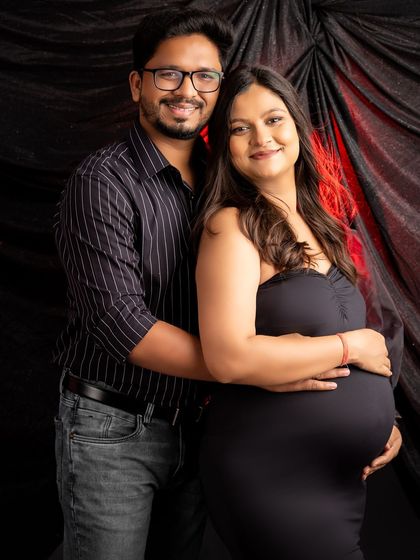 A happy and relaxed couple's portrait in the dark and moody style. They smile warmly for the camera, with a hint of red light adding dimension to the dark background.
