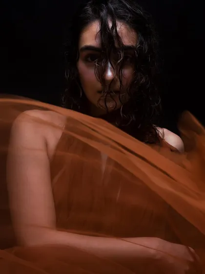 A close-up portrait where the wet, curly hair partially obscures the face, adding a sense of mystery. The makeup remains focused on a dewy, natural-looking glow.