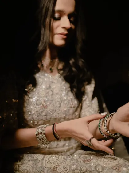 A close-up of the bride adjusting her bangles, with soft lighting highlighting the sparkle of her outfit.
