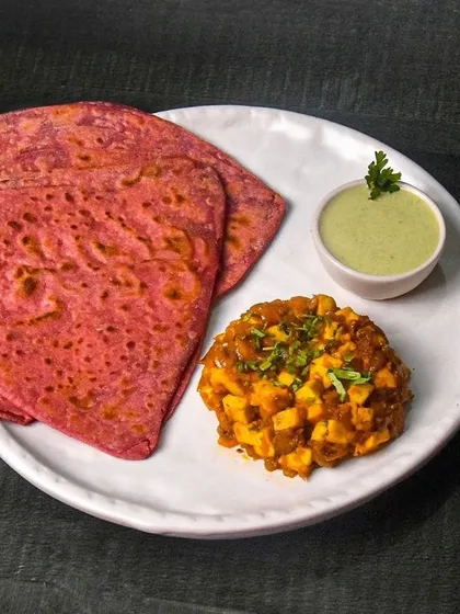Another angle of the beetroot paratha and paneer masala, showcasing the full plate. The dark, rustic table setting adds to the authentic feel of the dish.