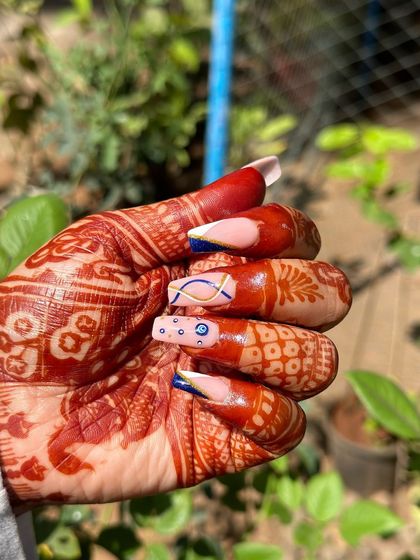 A beautiful bridal set with intricate henna-stained hands. The nails feature a modern French tip with an evil eye design, showing how students can cater to cultural trends.